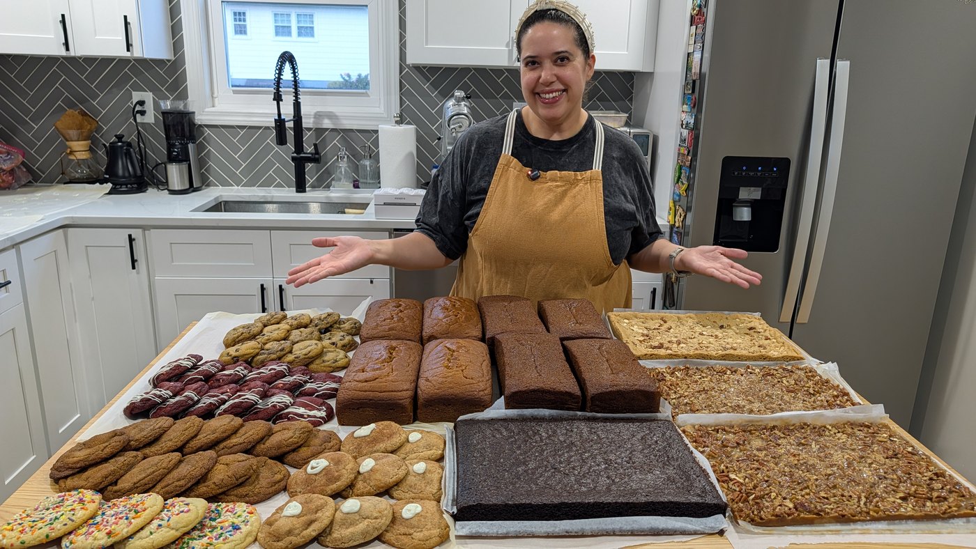 Renata behind a kitchen counter covered with homemade cookies, pound cakes, brownies, and bar cookies